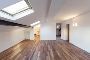 Dark brown hardwood flooring in a modern loft with smooth white walls and a large skylight flooding the space with natural light.