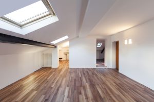 Dark brown hardwood flooring in a modern loft with smooth white walls and a large skylight flooding the space with natural light.